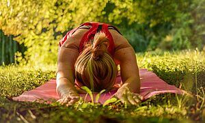 Yoga-Workshop zum Weltyogatag Frau macht Yoga auf einer Matte draußen im Grünen