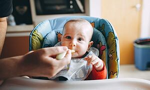 Ausgewogene Ernährung rund um die Schwangerschaft Baby im Hochstuhl wird gefüttert
